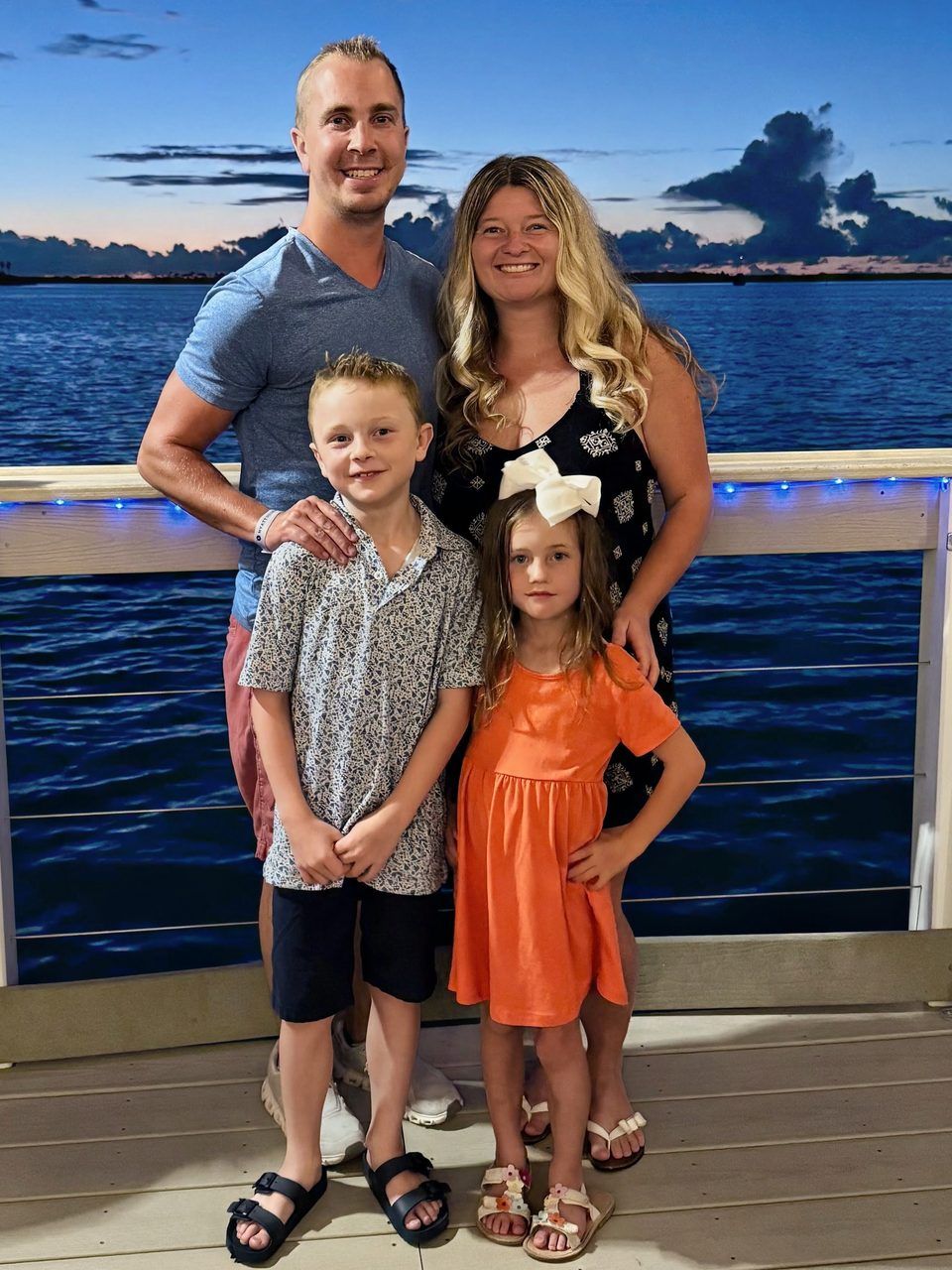 Nick Walters with his family, standing together at a railing by the water at dusk